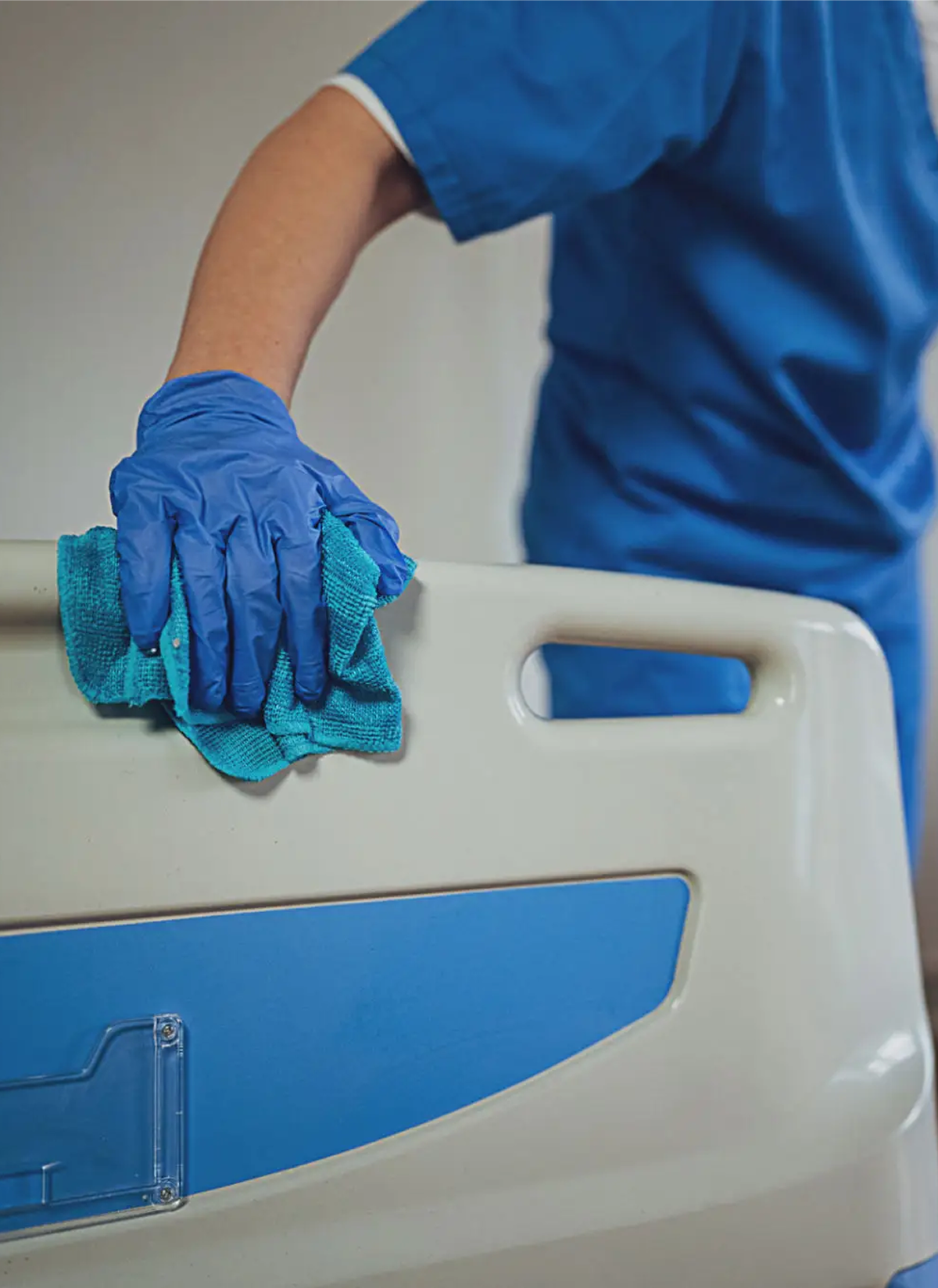 Person cleaning a hospital bed rail with a cloth and gloves.