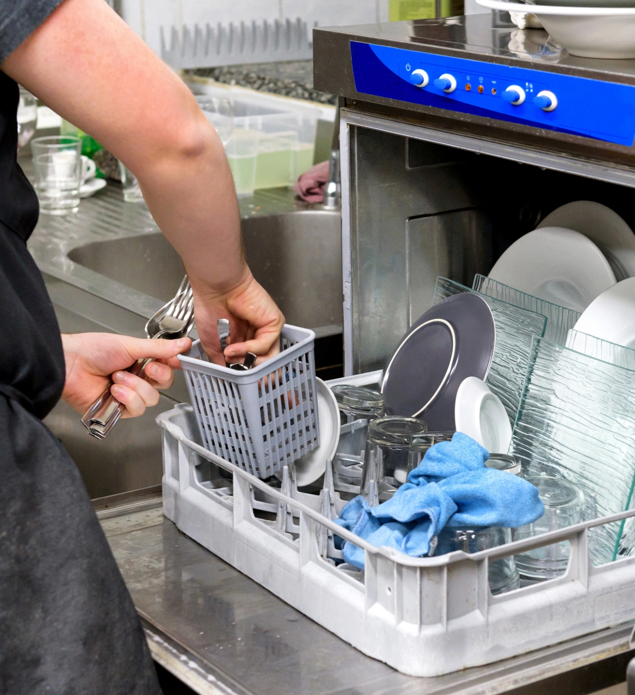Person loading utensils into a dishwasher's utensil basket.
