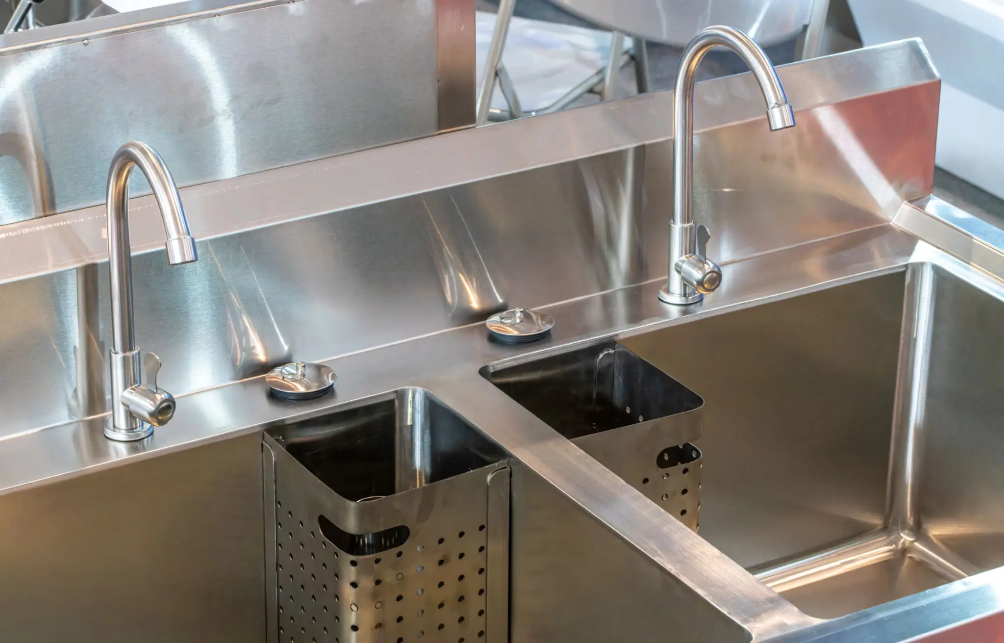 Metal kitchen sink station with two basins and built-in soap dispensers.