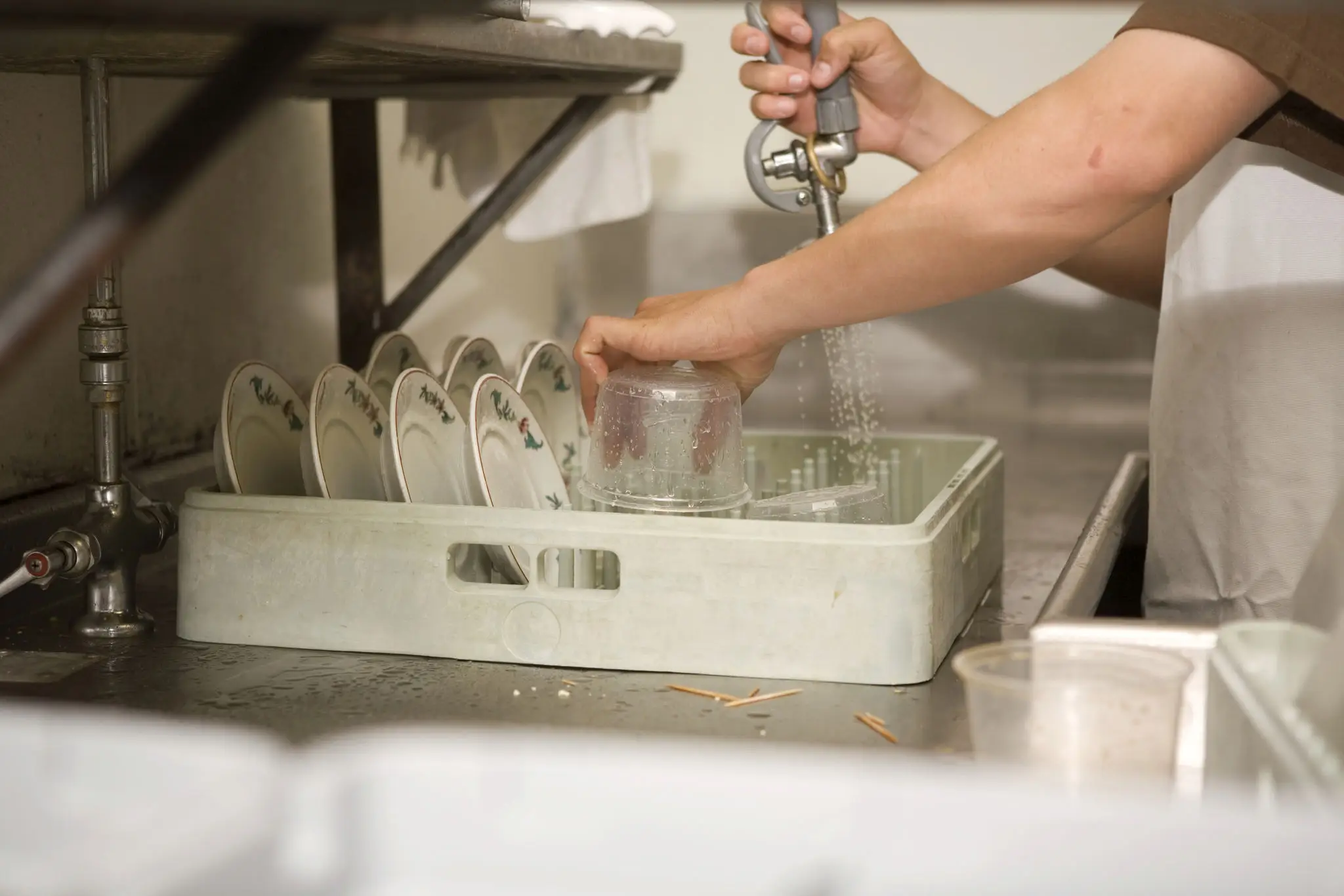 Hand washing dishes in a commercial kitchen sink.